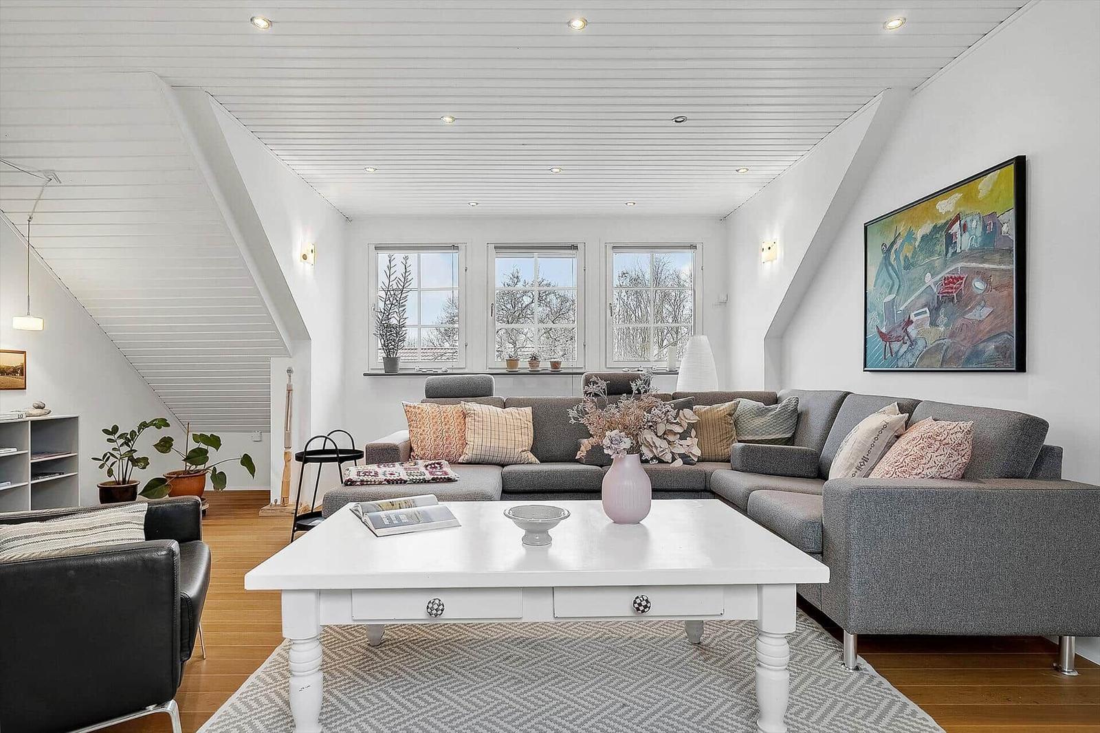 Wohnzimmer mit grauem Sofa, weißem Tisch und Fenstern.