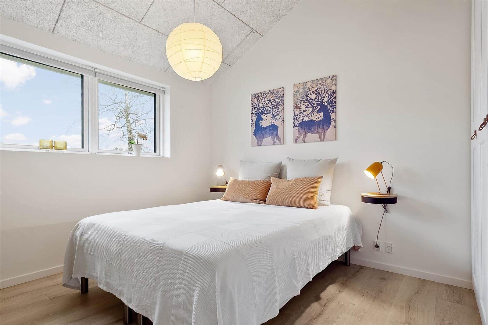 Schlafzimmer mit Bett, Fenster und Wandbildern.