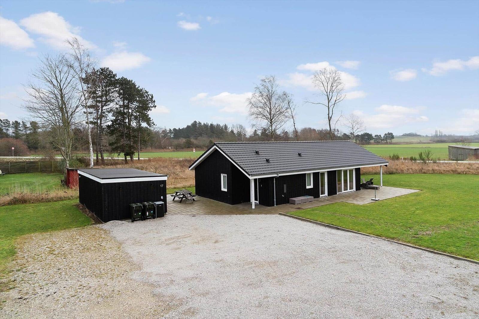 Schwarzes Ferienhaus mit Terrasse und Garten. Grasfläche und Wald im Hintergrund.