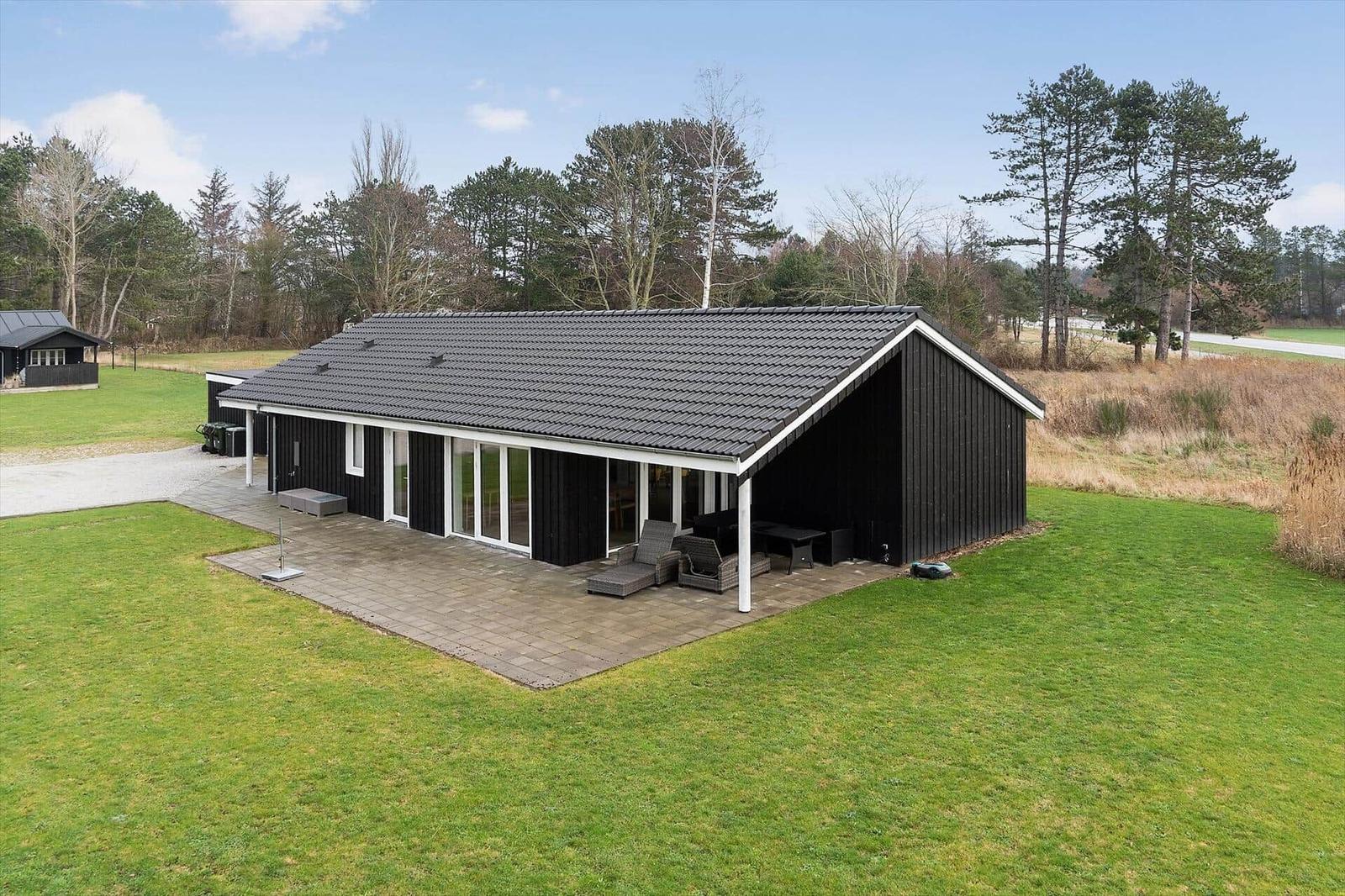 Modernes Haus mit Terrasse und Garten. Umgeben von Bäumen und Gras.