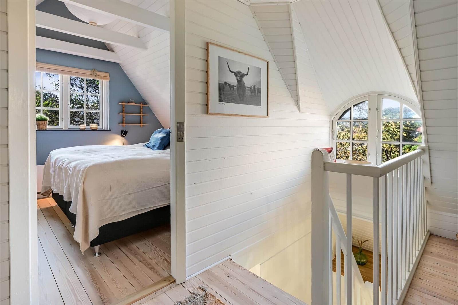 Schlafzimmer mit Bett und Fenster. Treppenhaus mit Geländer und Wandbild.