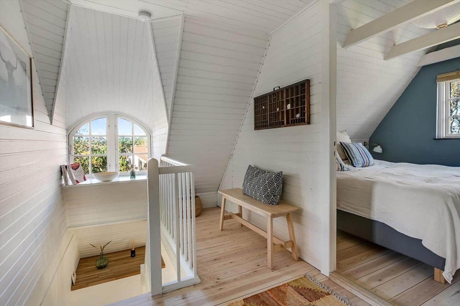 Schlafzimmer mit Dachschräge, Bett, Fenster und Holzboden.