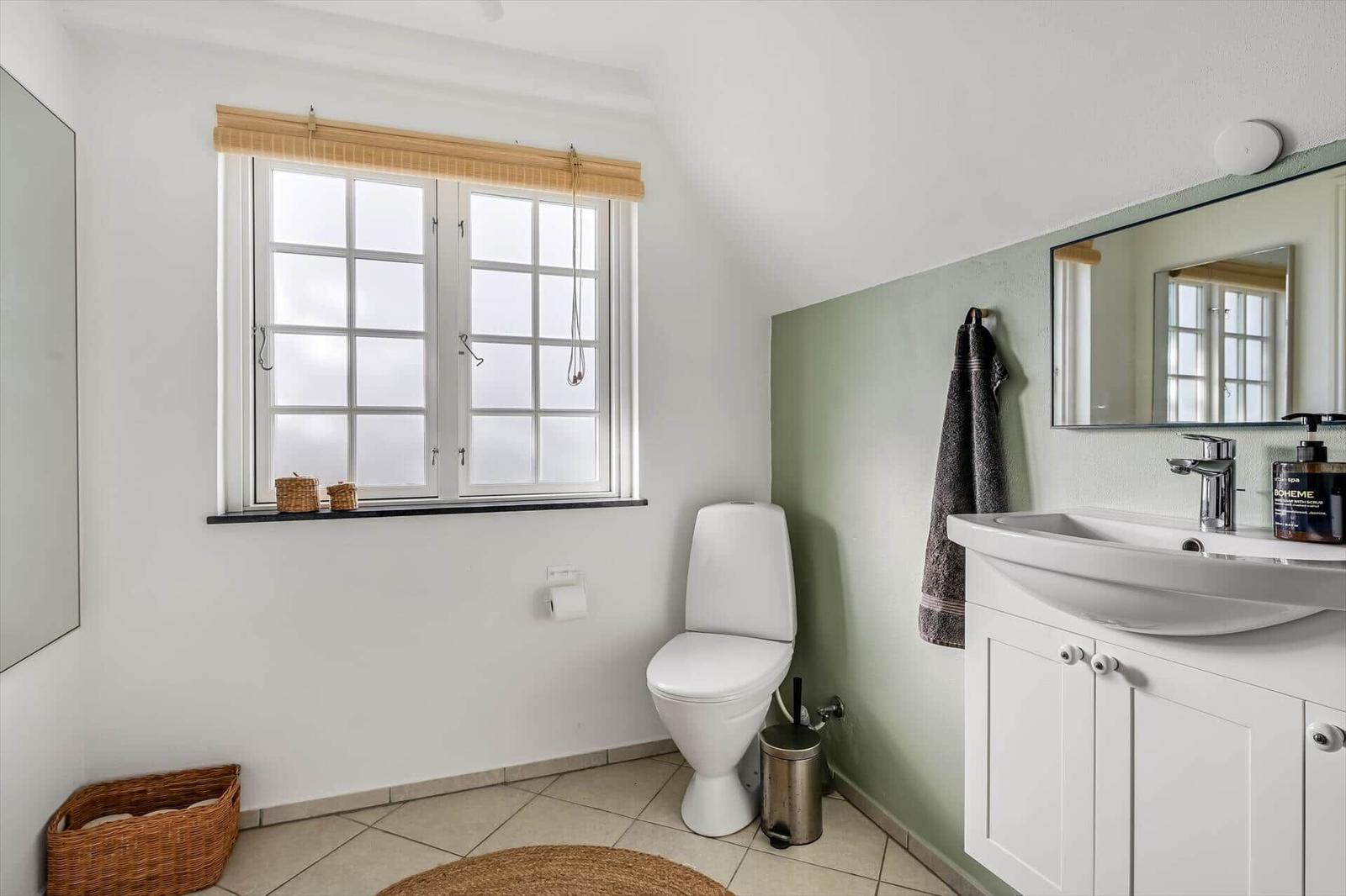 Badezimmer mit Toilette, Waschbecken und Fenster mit Jalousie.