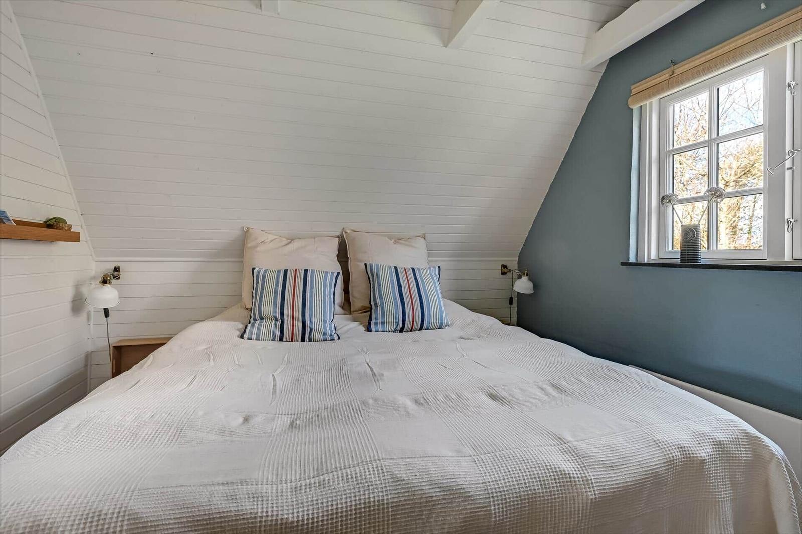 Schlafzimmer mit Dachschrägen, weißer Wand, Bett und Fenster mit Blick.