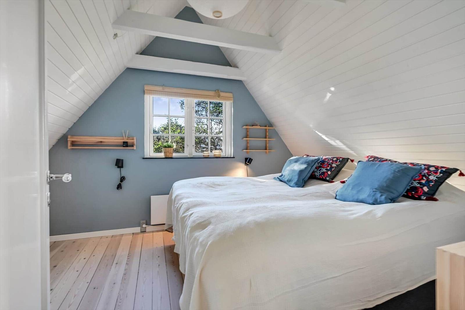 Schlafzimmer mit Dachschrägen, Bett, Fenster und Holzboden.
