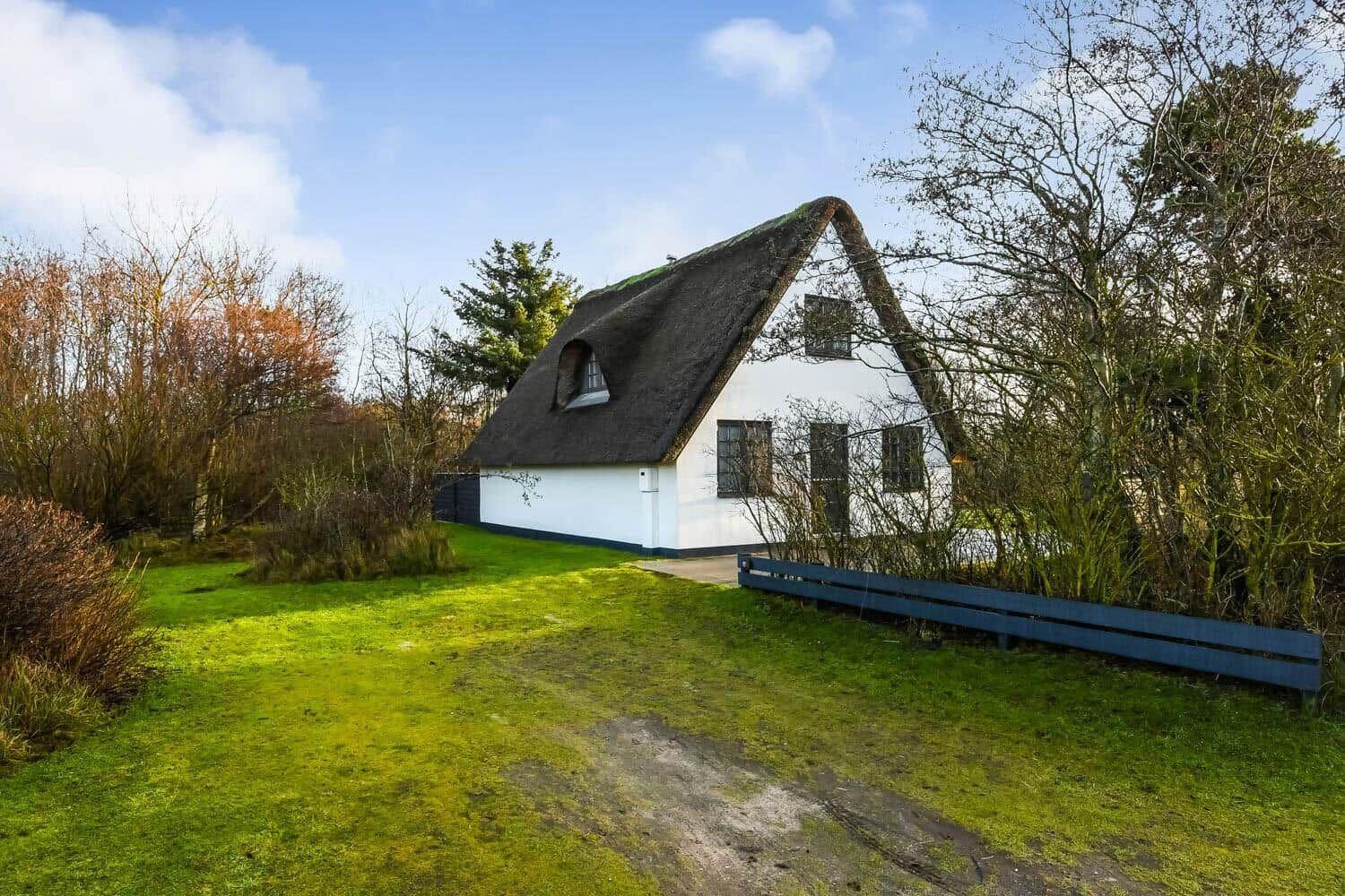 Ein weißes Haus mit strohgedecktem Dach steht auf einer grünen Wiese.