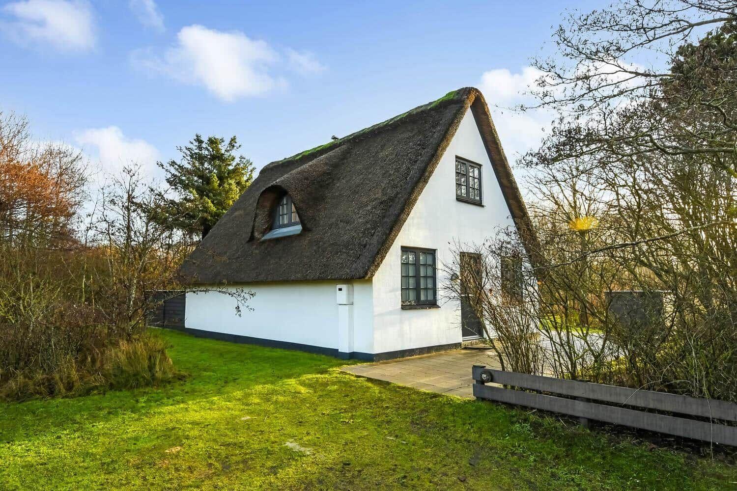 Ein weißes Haus mit strohgedecktem Dach und mehreren Fenstern steht auf grünem Grund.