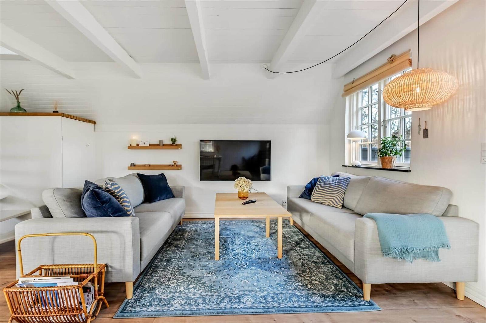 Wohnzimmer mit zwei Sofas, Holztisch und blauem Teppich unter hohem Dach