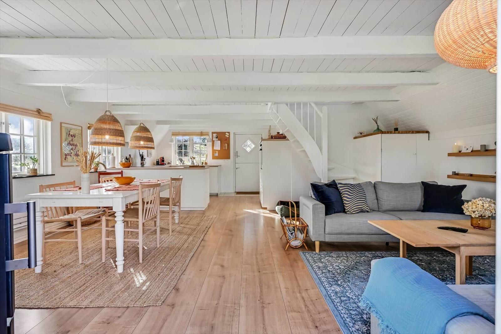 Wohn- und Essbereich mit Holzboden, Sofa und Tisch. Weiße Wände und Decke mit Holzbalken.