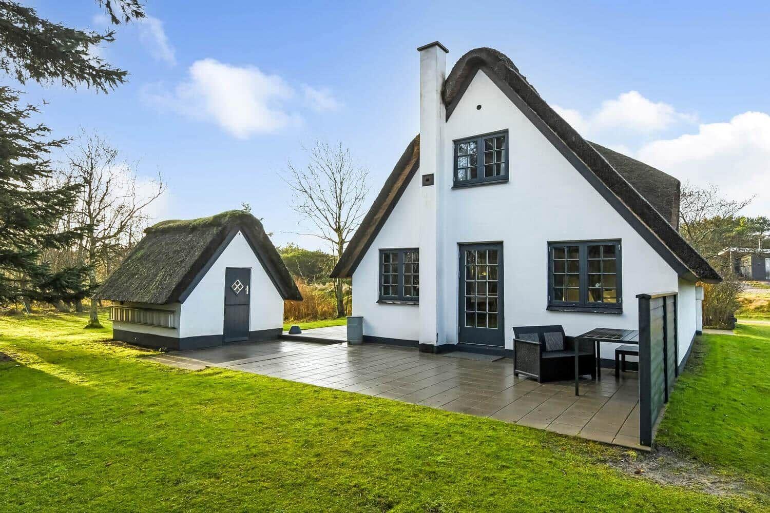 Weiße Häuser mit Strohdächern und Terrasse im Garten.