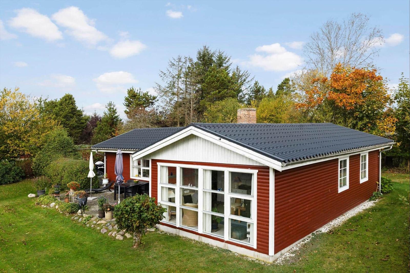 Red wooden house with large window area and garden area with terrace.