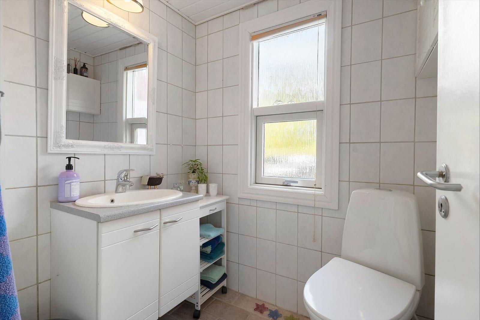 Bathroom with sink, mirror, toilet, and window.
