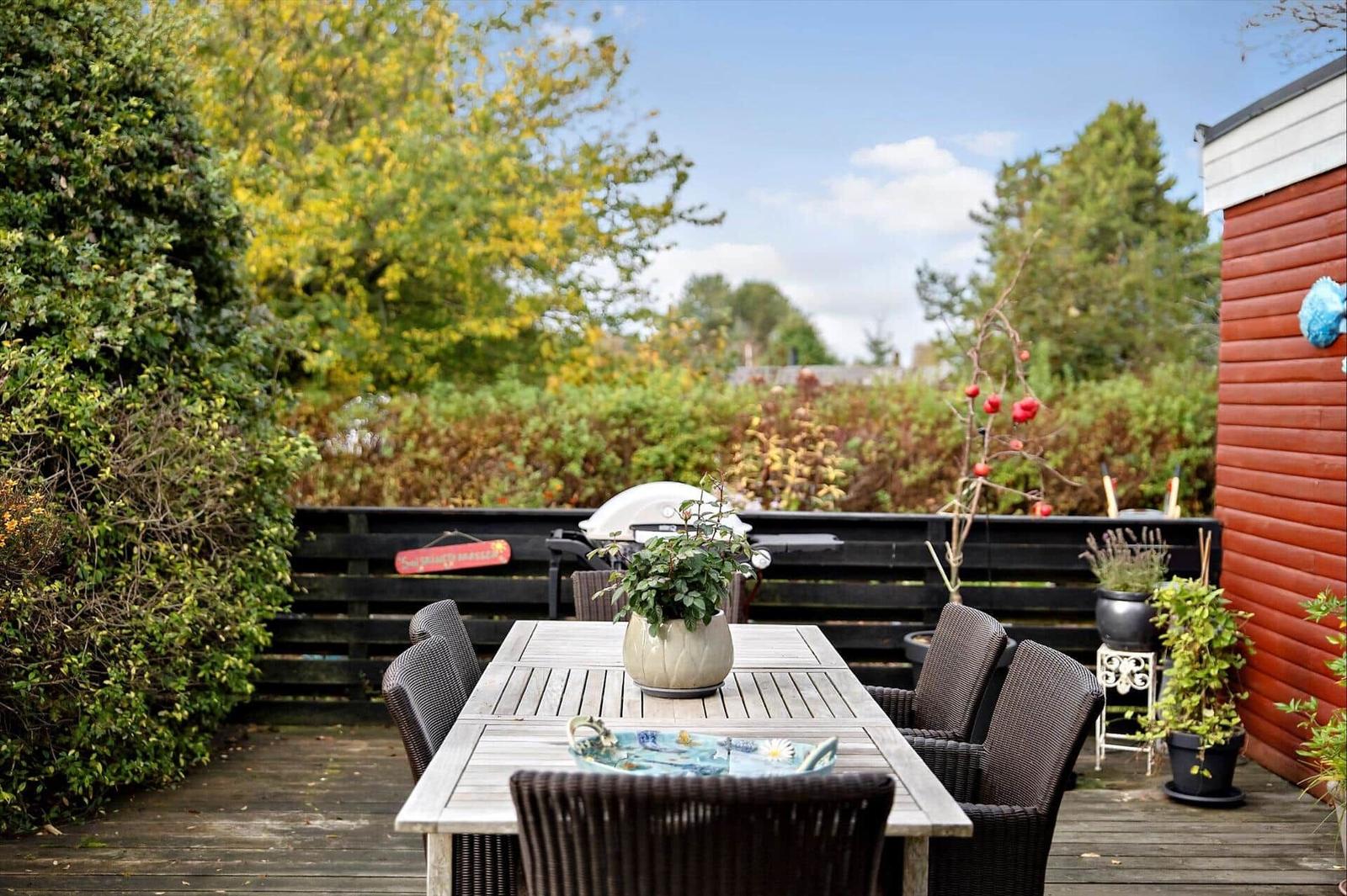 Deck with table, chairs, and grill. Surrounded by plants and trees.