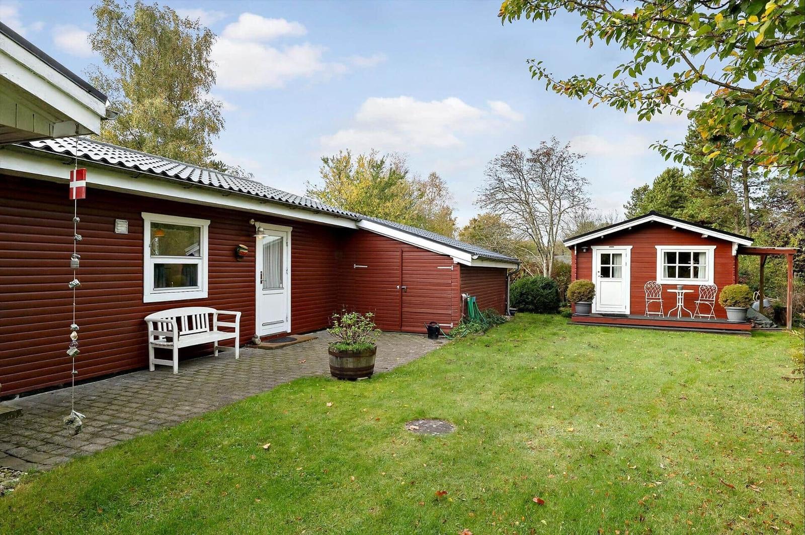 Red wooden house with white veranda and garden. Backyard with table and chairs.