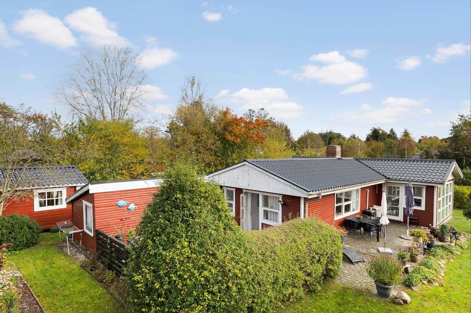 Red house with garden and terrace under blue sky.