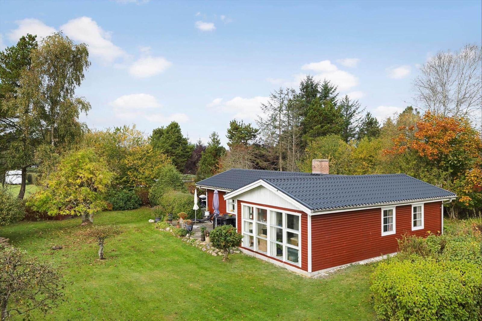 Red house with garden and terrace under blue sky.