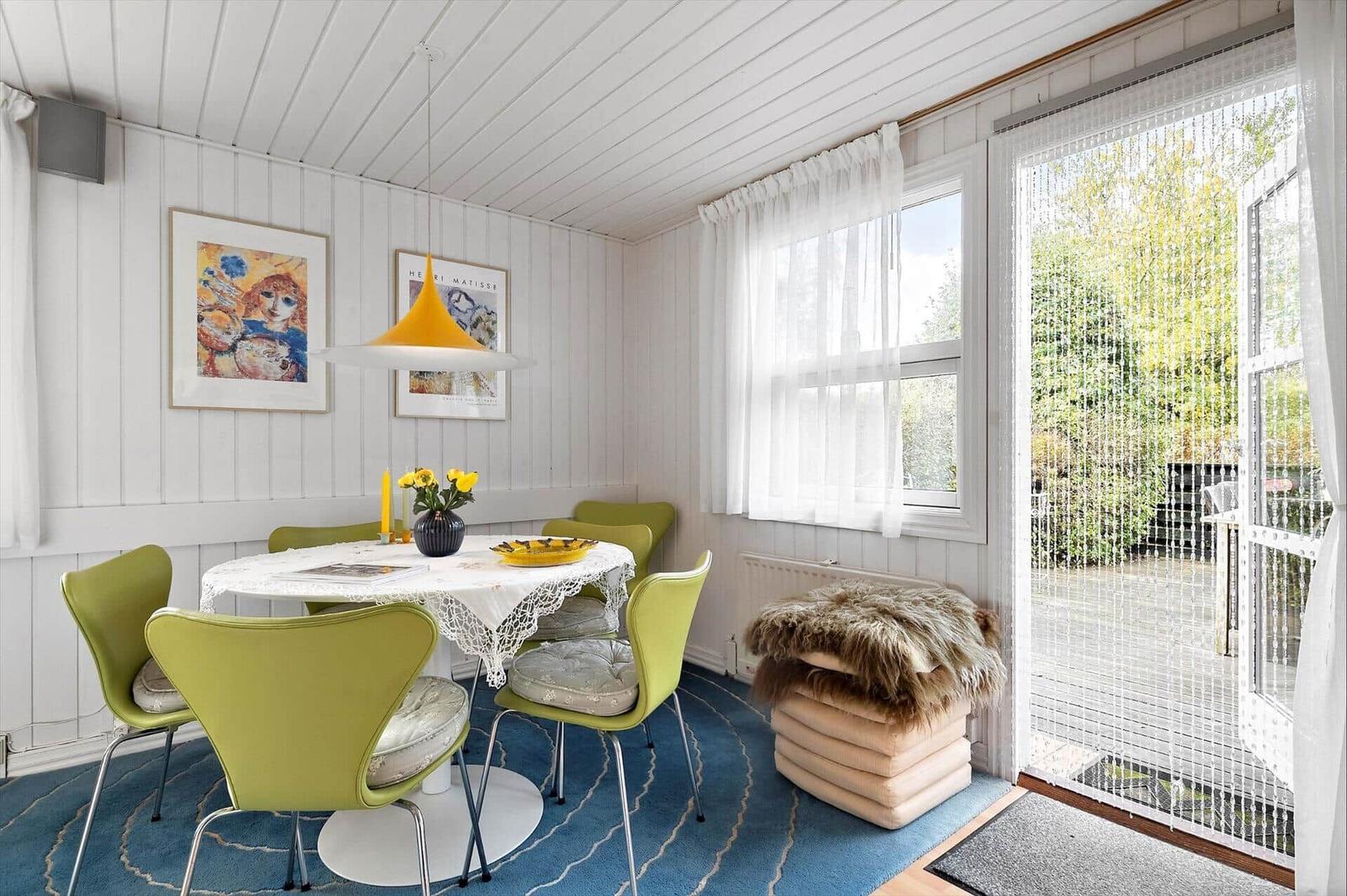 Dining room with green chairs, white table, and blue rug. Access to terrace.