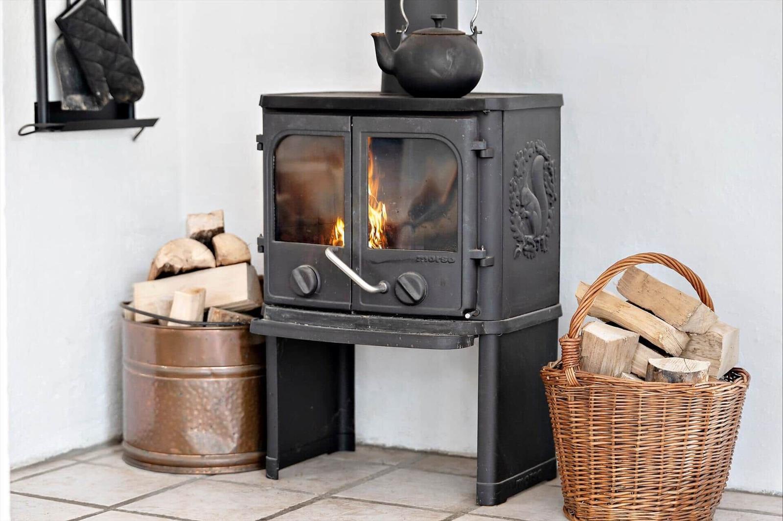 Black wood-burning stove with fire, metal bucket, and wicker basket with firewood.