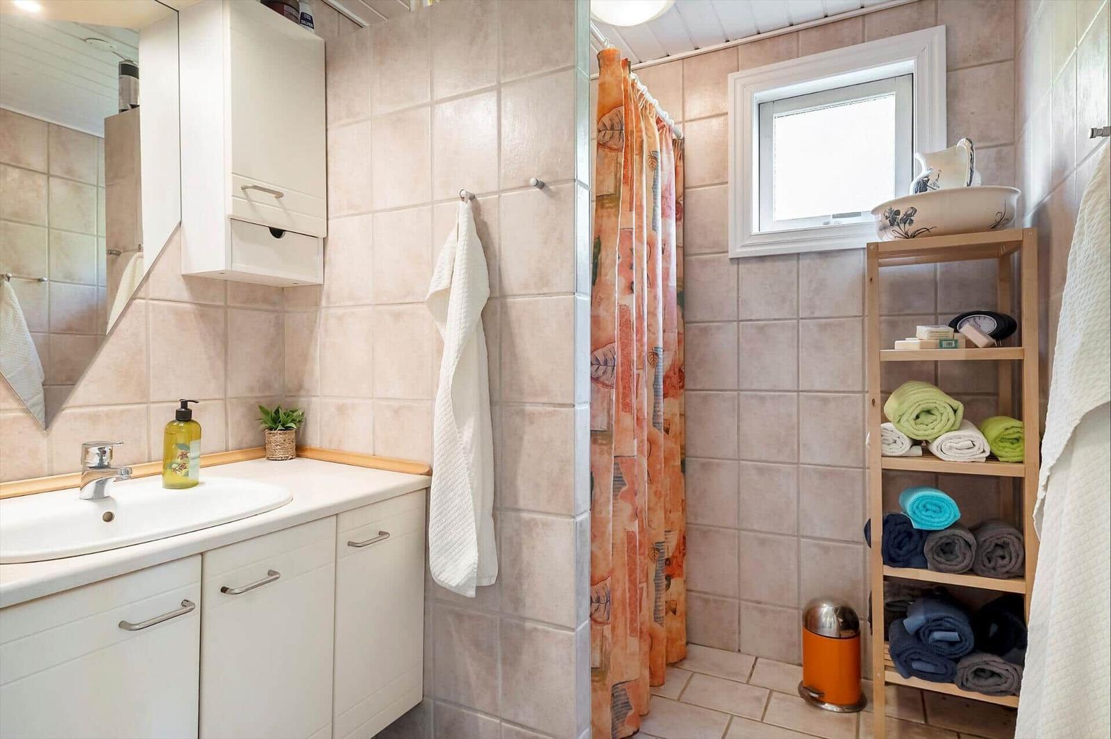 Bathroom with sink, shower, and wooden shelf with towels.