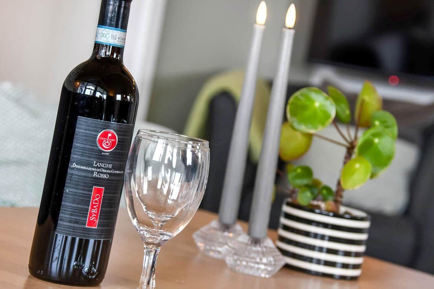 Eine Weinflasche und ein Glas stehen auf einem Tisch neben Kerzen und einer Pflanze.
