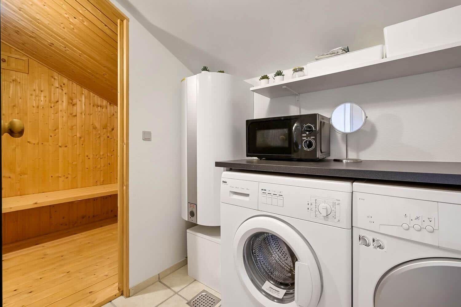 Wäscherei mit Waschmaschine und Trockner, Mikrowelle und Sauna im Hintergrund.
