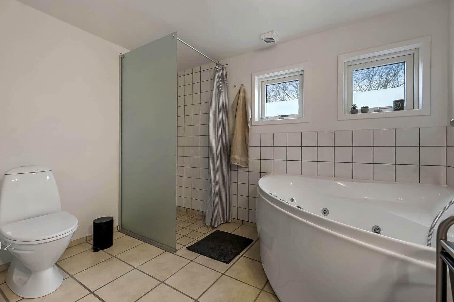 Badezimmer mit Badewanne, Dusche und Toilette. Fenster mit Blick nach draußen.
