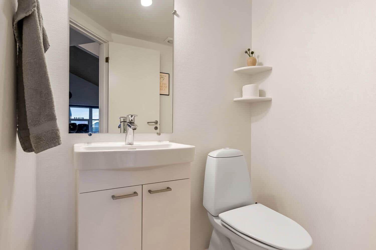Badezimmer mit Waschbecken, Spiegel, Toilette und Handtuch.