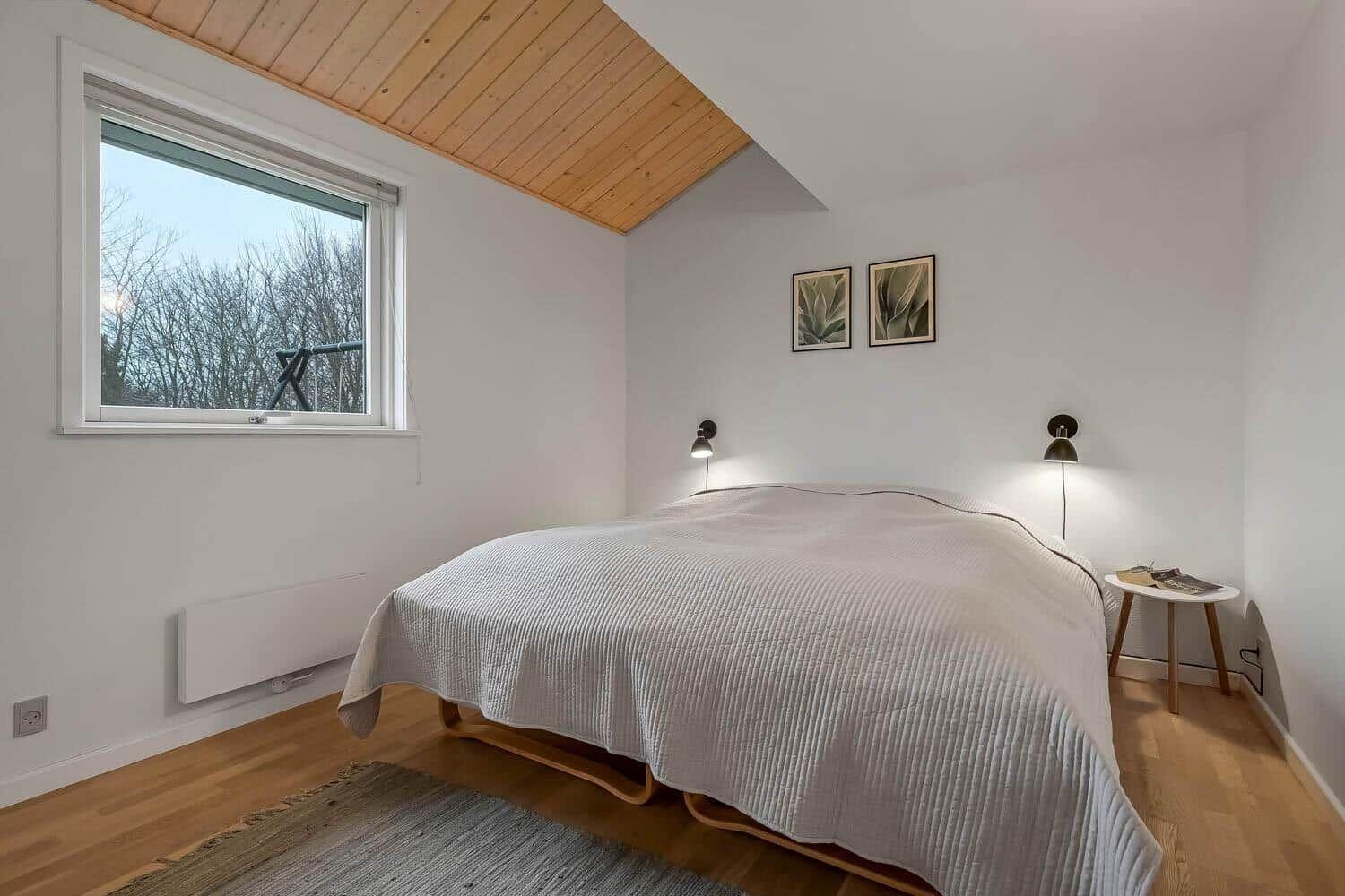 Schlafzimmer mit Bett, Fenster und Holzdecke.