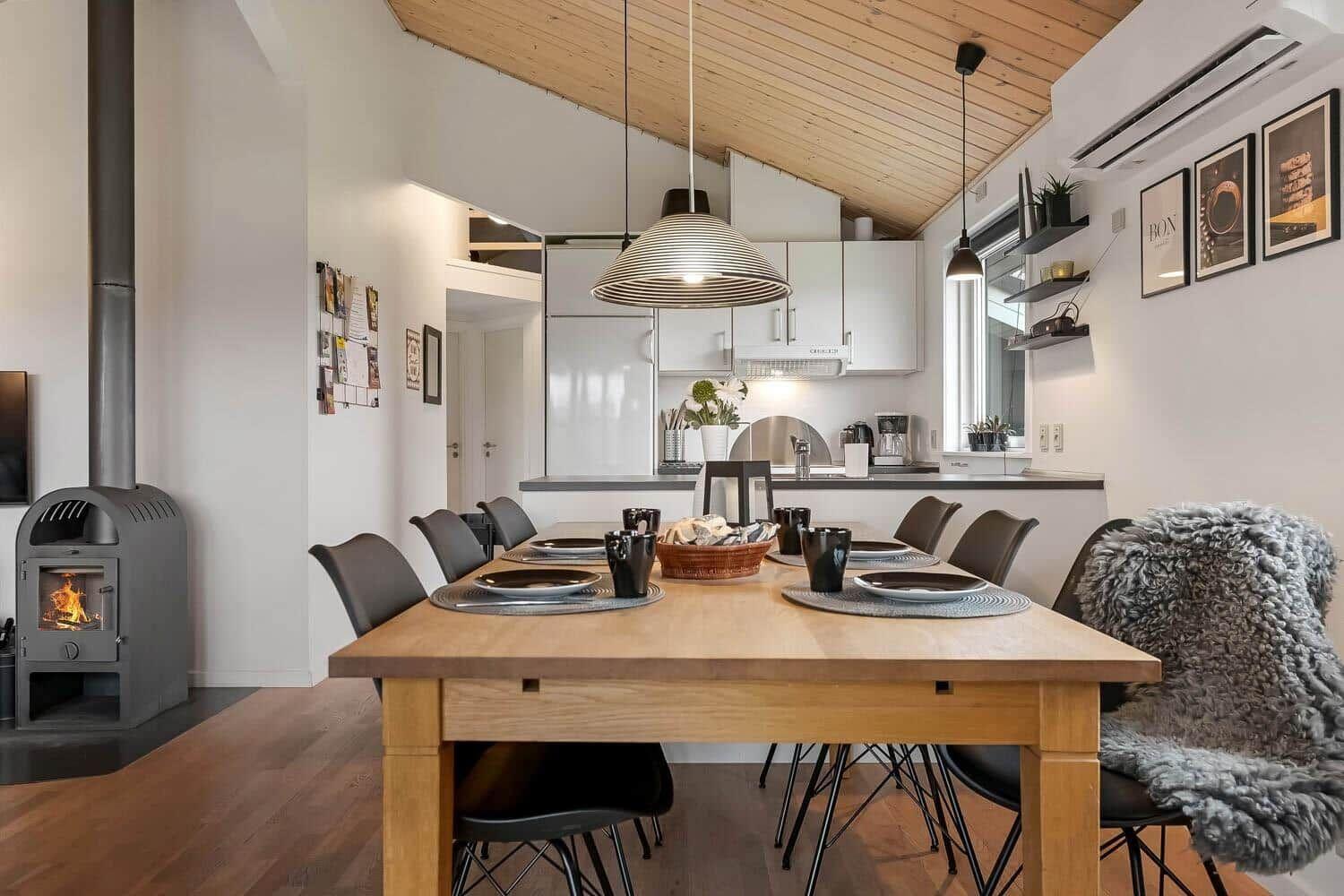 Essbereich mit Holztisch, Stühlen und Kaminofen. Küche im Hintergrund.