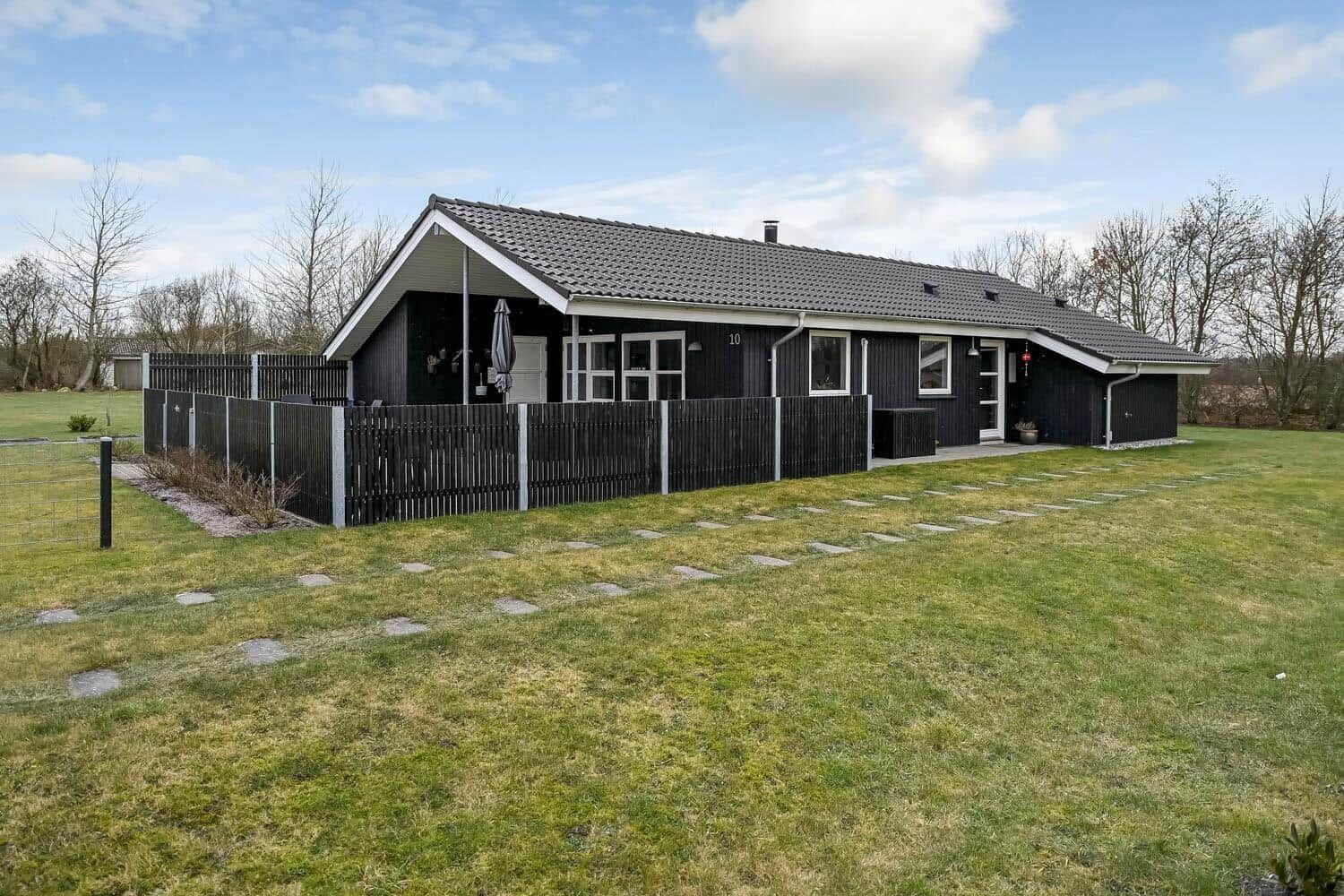 Ein modernes Haus mit schwarzer Fassade und weißem Dachrand. Umgeben von Gras und einem Zaun.