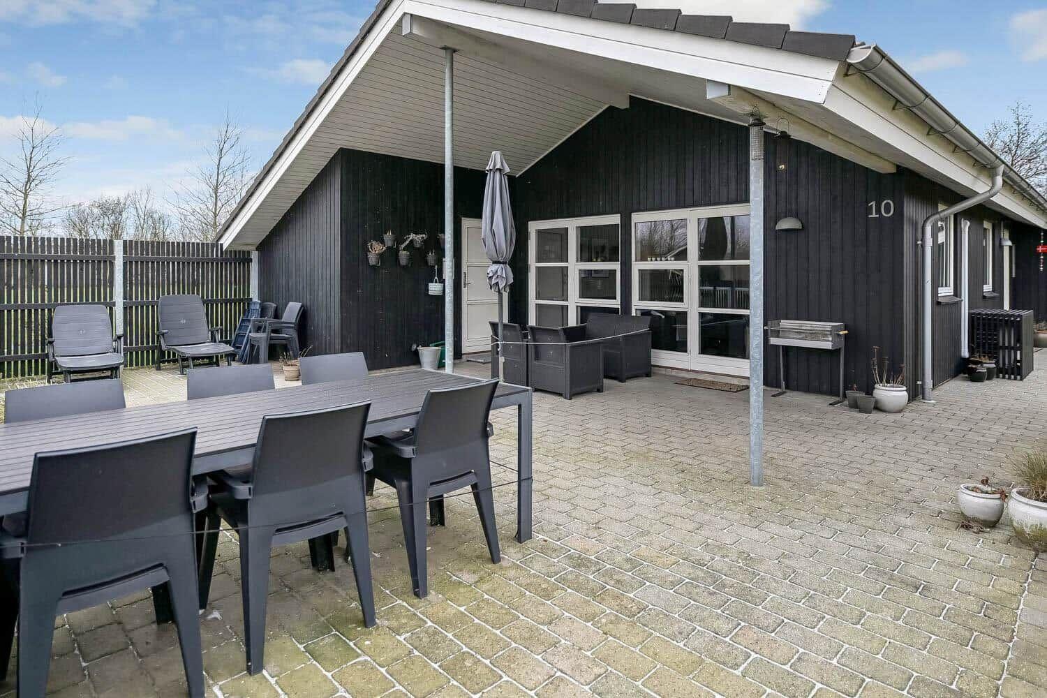 Außenbereich mit Tisch, Stühlen und Grill. Schwarze Holzwand und Terrasse.