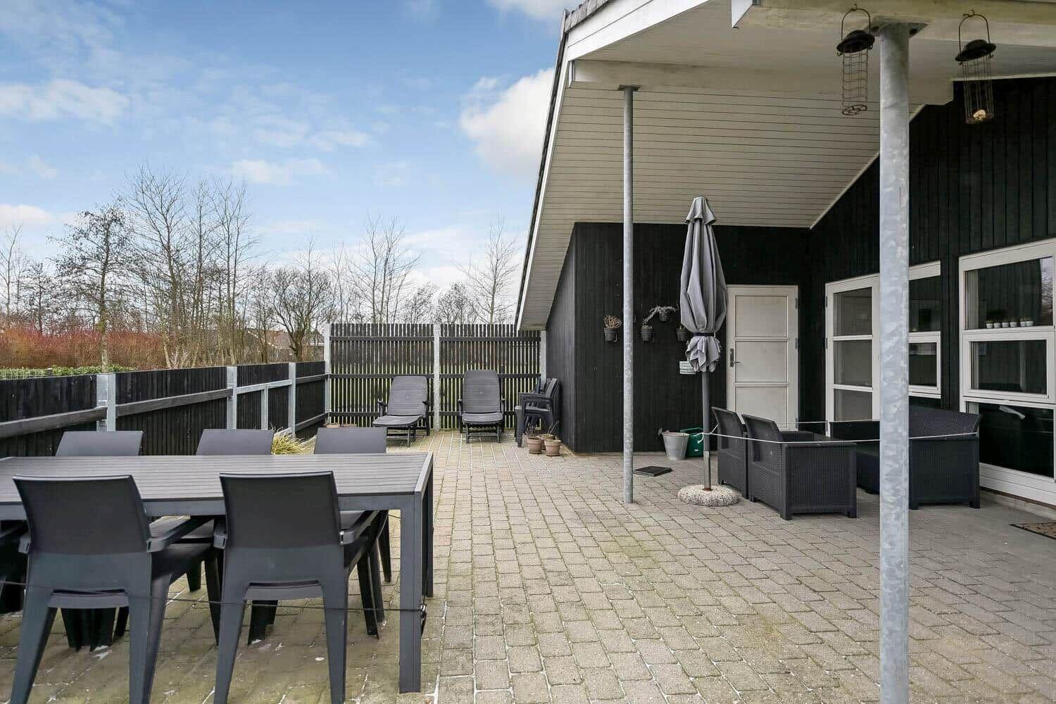 Terrasse mit Tisch, Stühlen und Liegestühlen. Hinterhof mit Zaun und Bäumen.