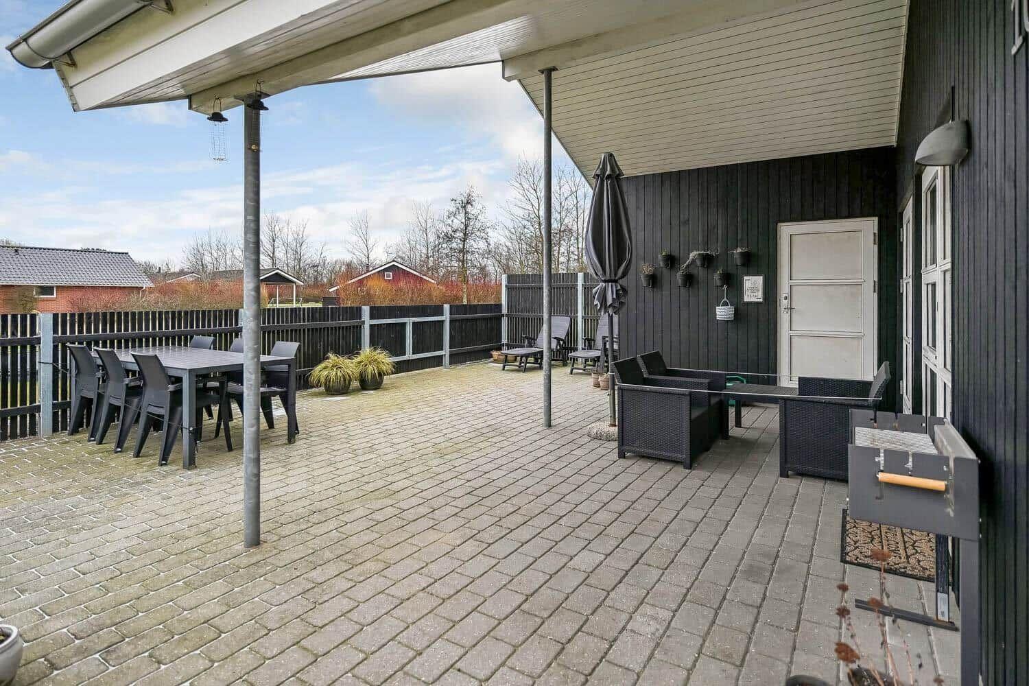 Terrasse mit Tisch, Stühlen und Sitzgruppe unter Markise. Grill und Pflanzen sind vorhanden.
