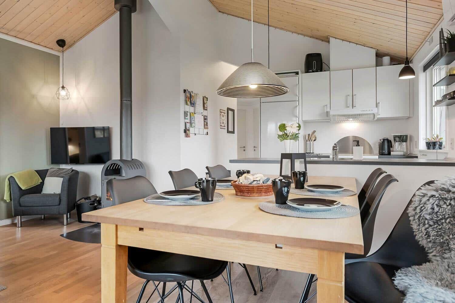Essbereich mit Holztisch, Küchenzeile und Kaminofen im Hintergrund.