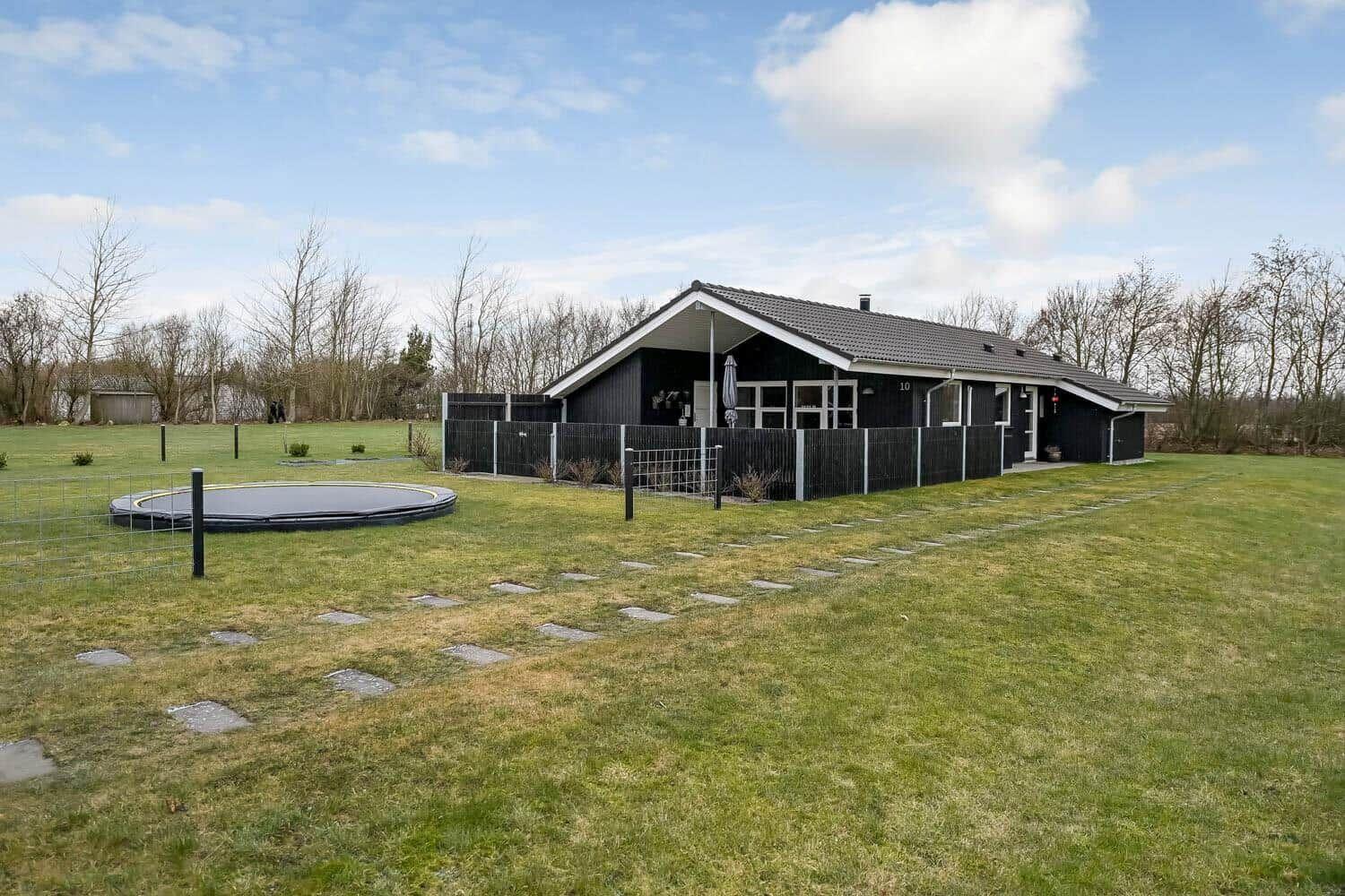 Schwarzes Ferienhaus mit Terrasse, umzäunter Garten und Trampolin.