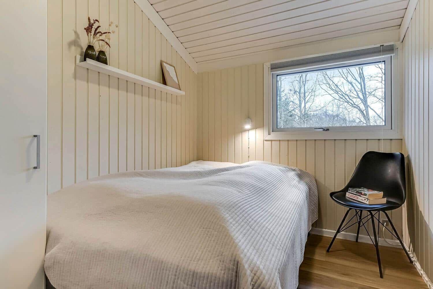 Schlafzimmer mit Bett, Fenster und schwarzer Stuhl.