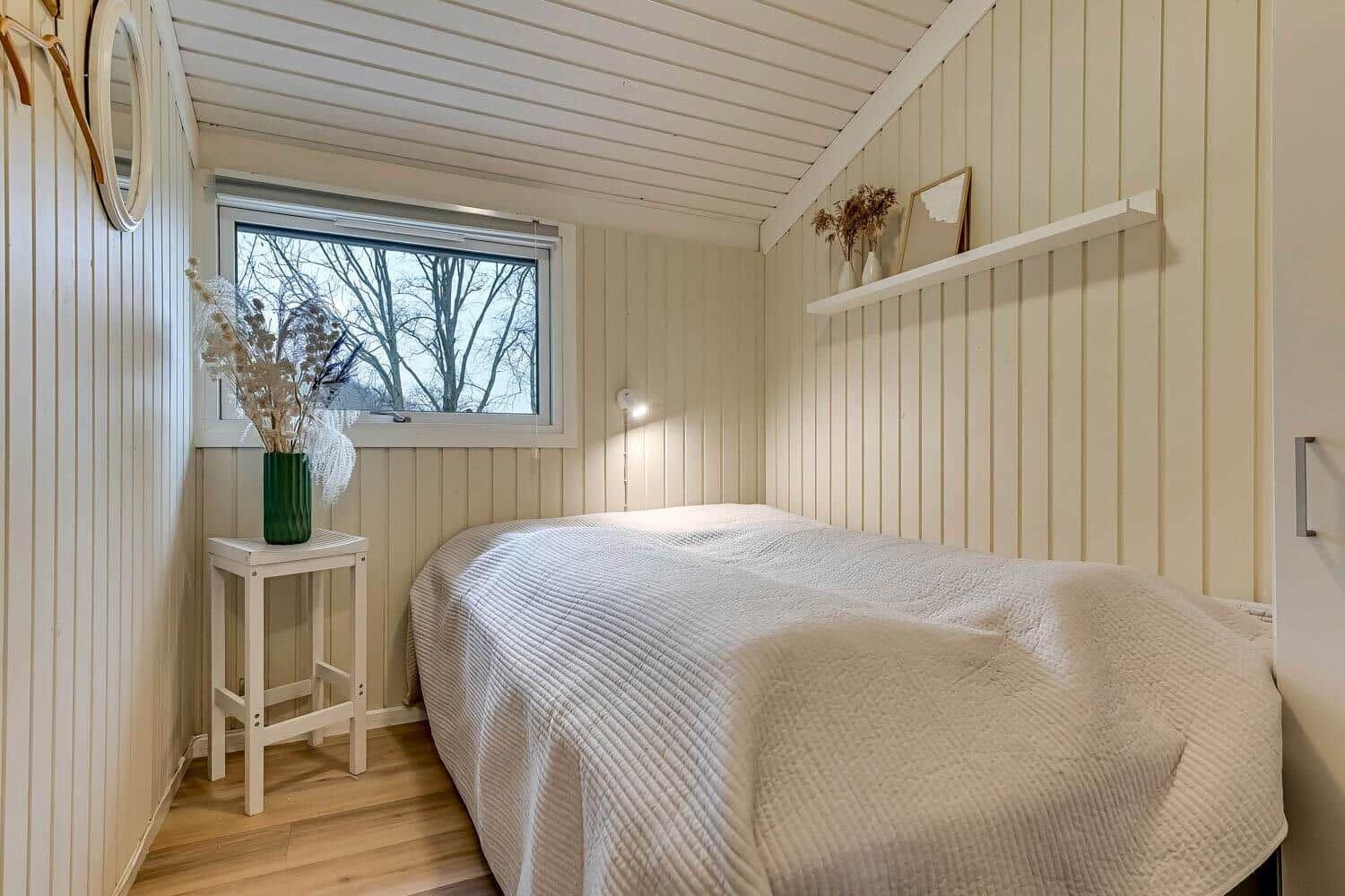 Schlafzimmer mit Bett, Fenster und kleinem Tisch mit Vasen.