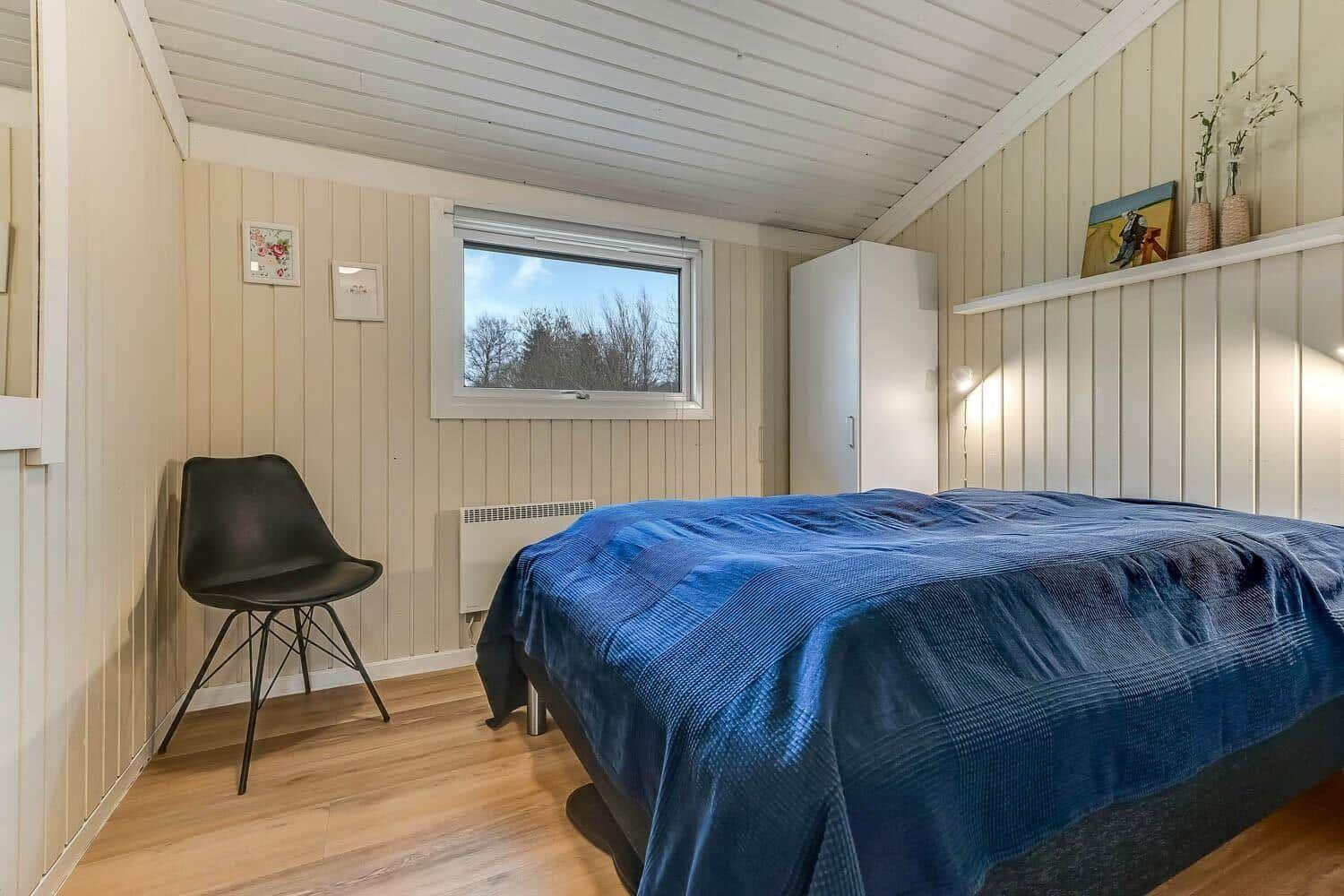 Schlafzimmer mit Bett, Fenster, Schrank und Stuhl.