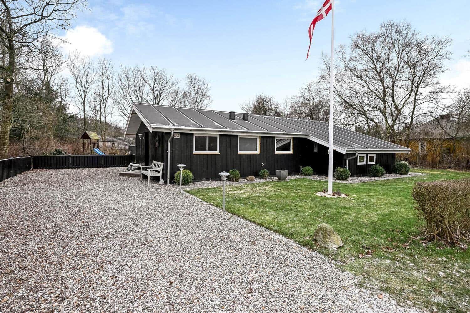 Schwarzes Holzhaus mit Garten, Flagge und Spielplatz. Gravierter Weg und Rasen.