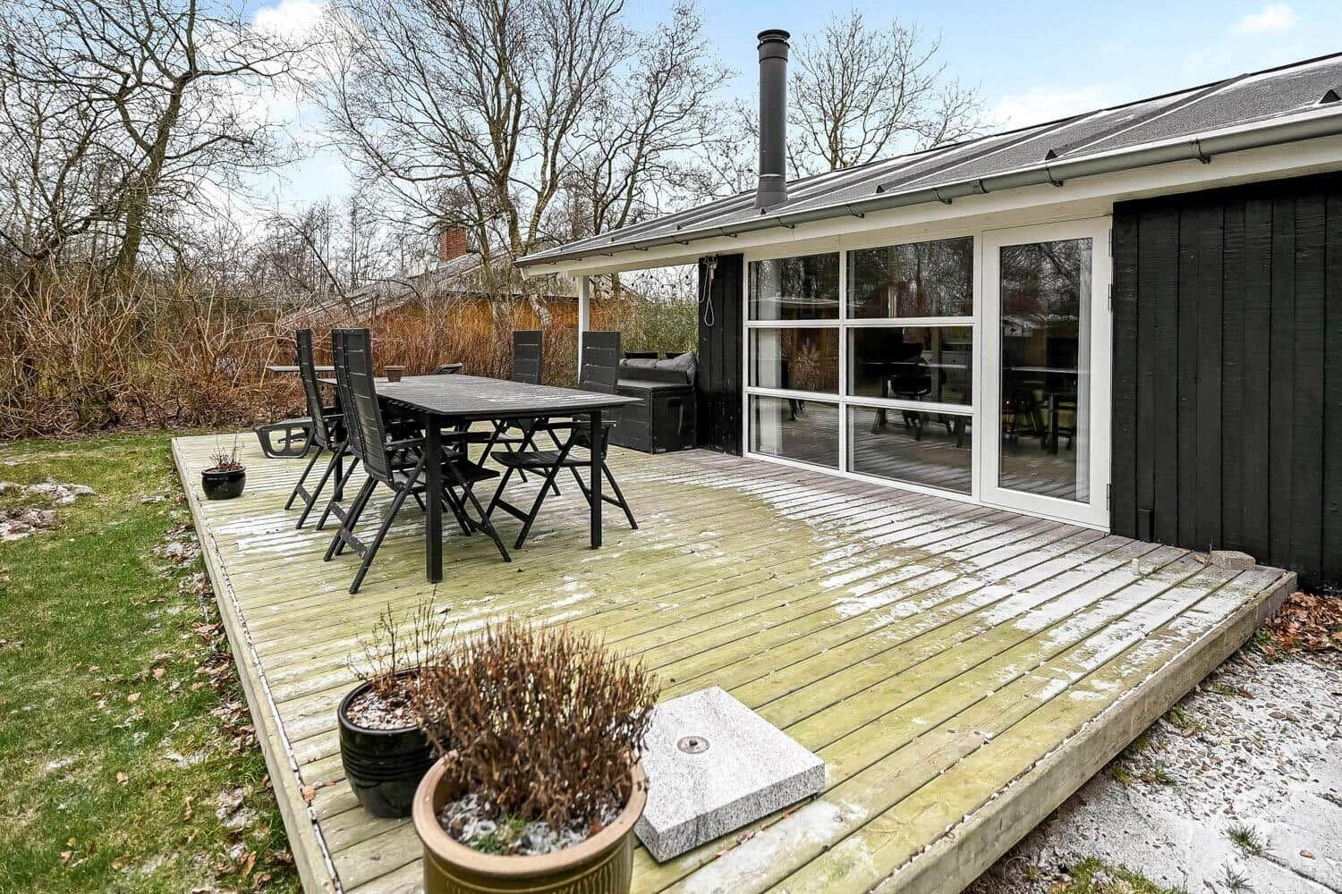 Terrasse mit Tisch, Stühlen und Grill. Glasfront führt ins Haus.