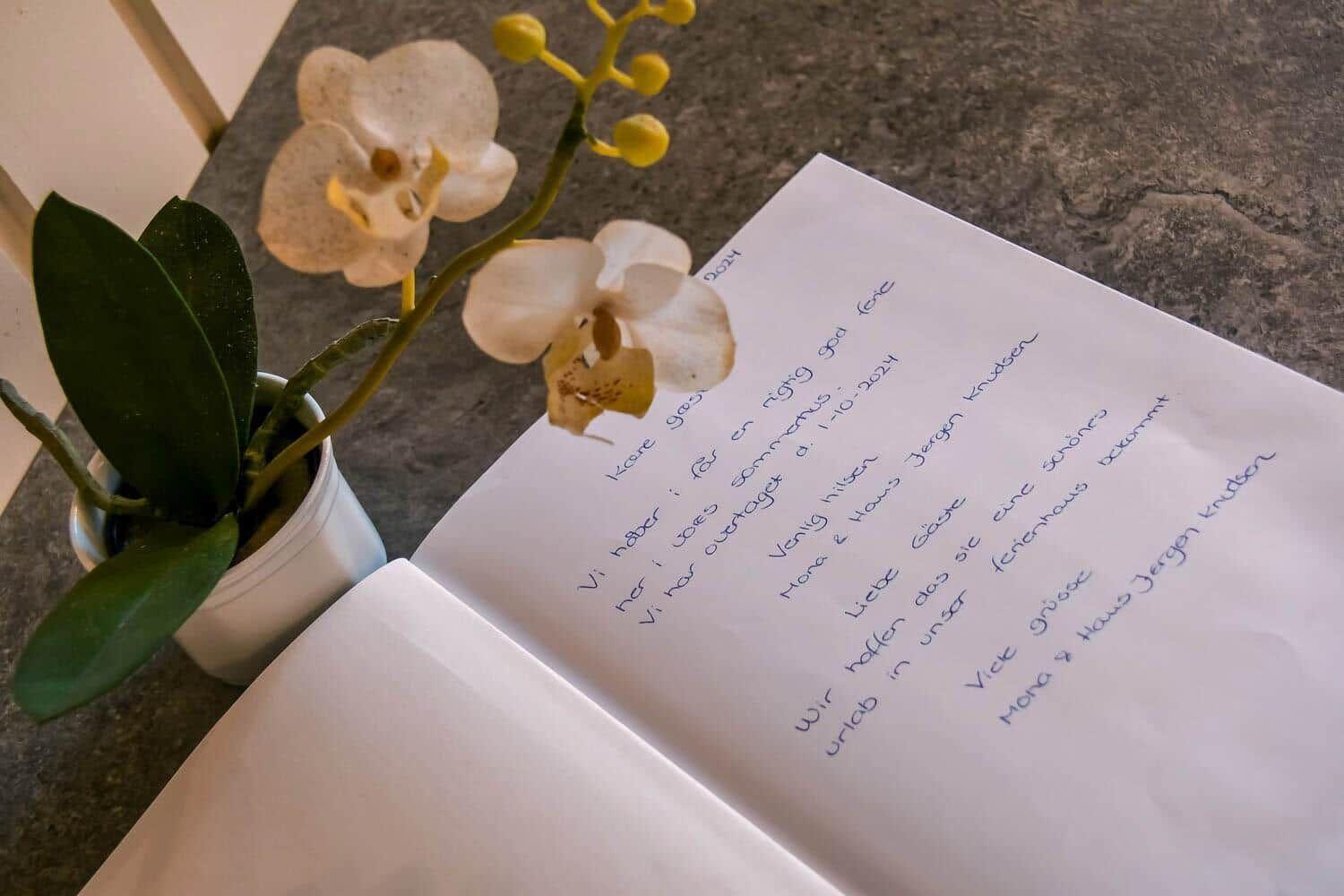 Ein Buch mit handschriftlichem Text und eine Orchidee auf einer Arbeitsfläche.