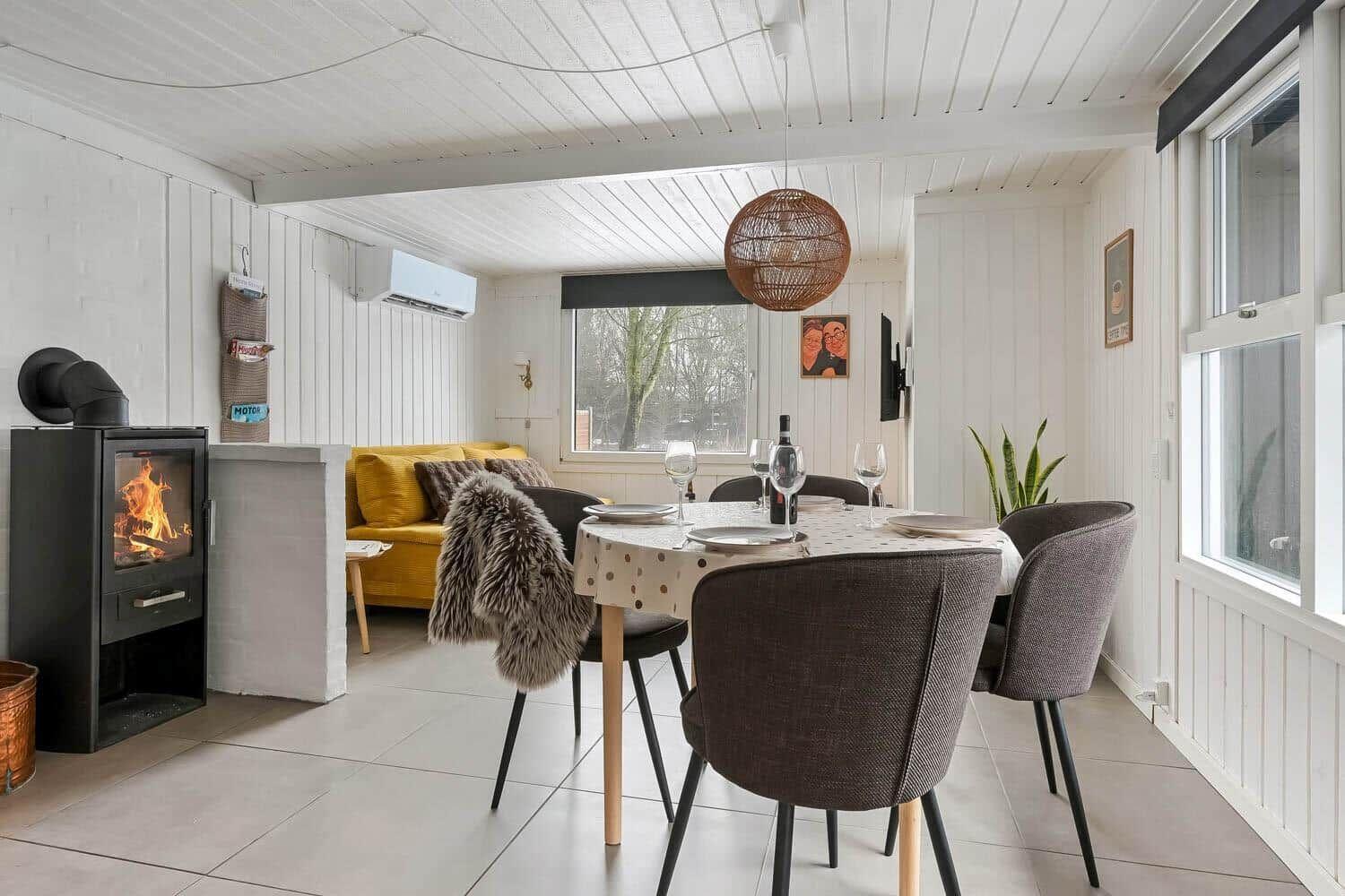 Esszimmer mit Esstisch, Stühlen und Kaminofen. Gelber Sofa im Hintergrund.