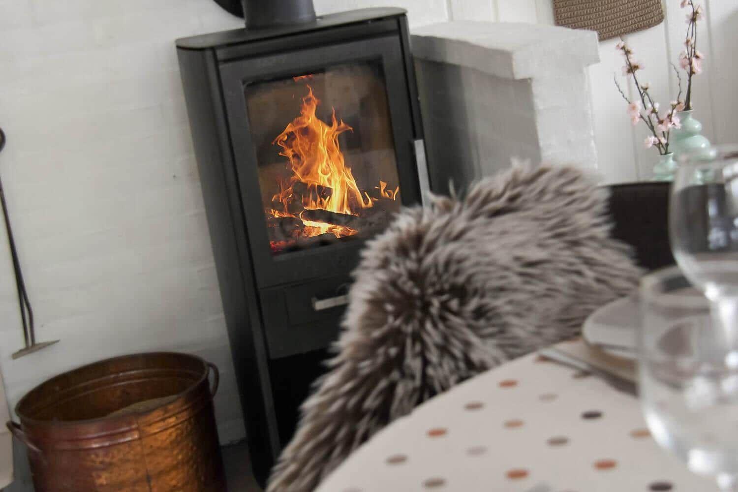 Holzofen mit brennendem Feuer, Tisch mit Polster und Glas