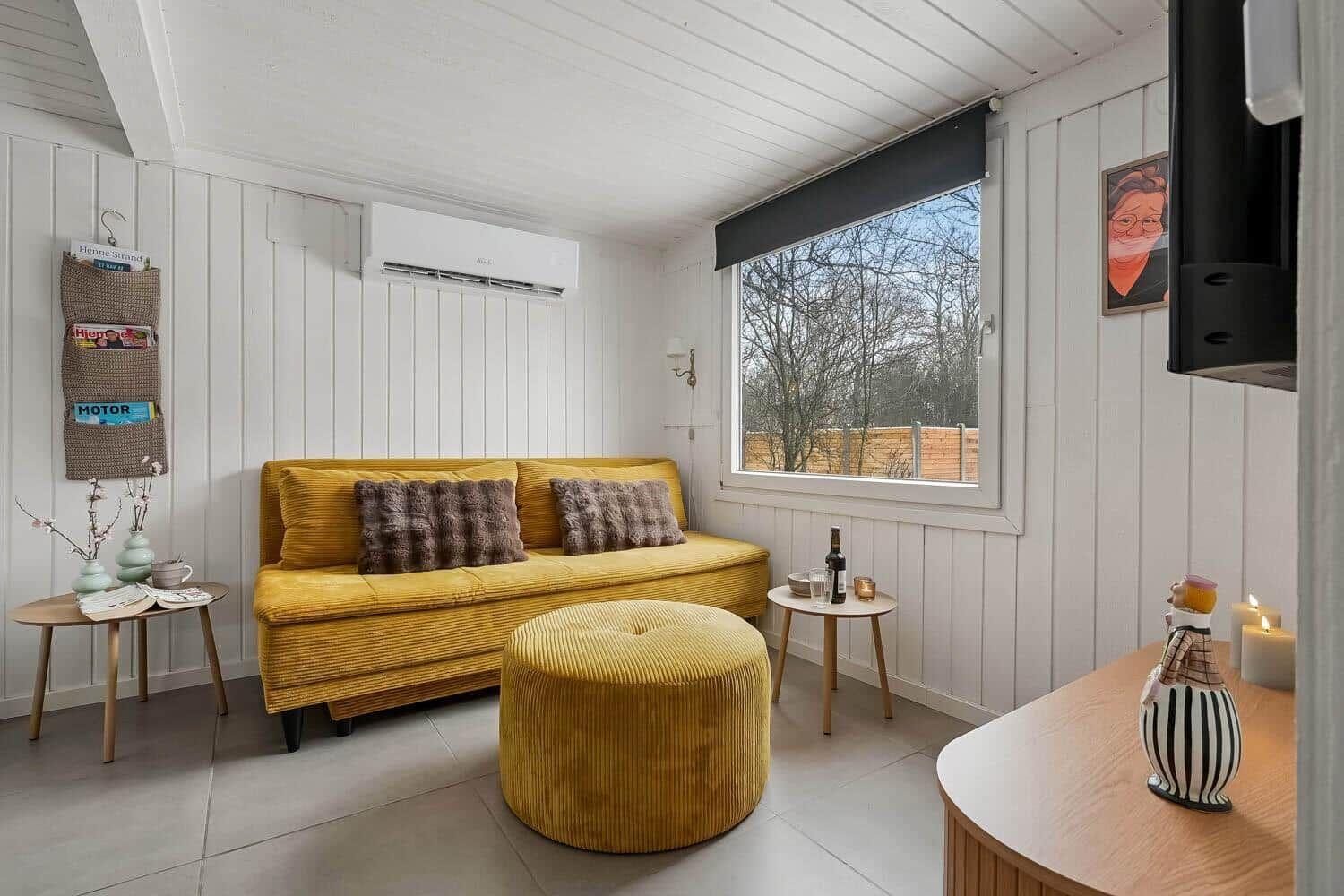 Gelber Sofa und Sitzhocker im Wohnbereich mit Fenster und Wandheizung.