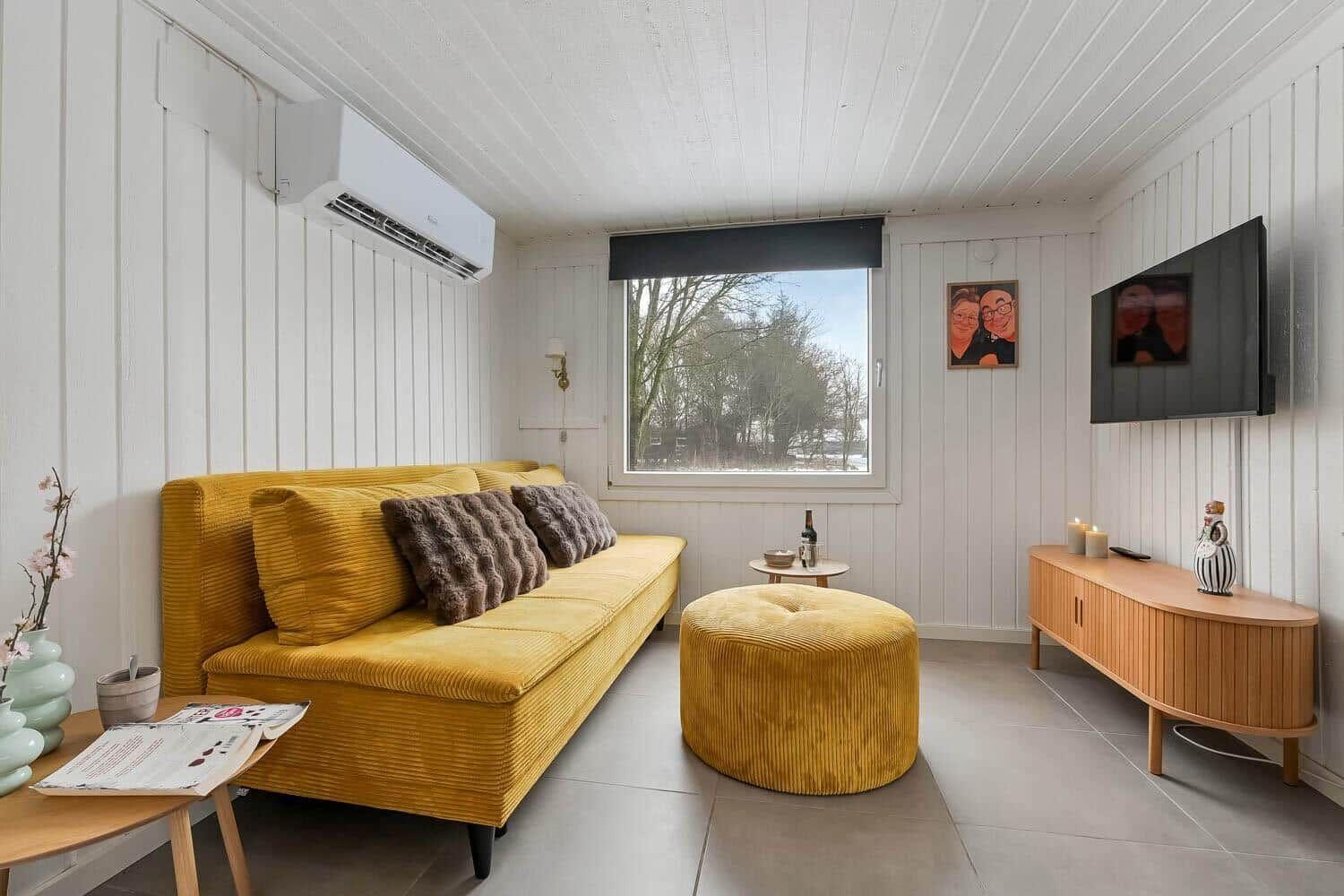 Ein Wohnzimmer mit gelbem Sofa, runden Sitzkissen und Holzmöbeln.