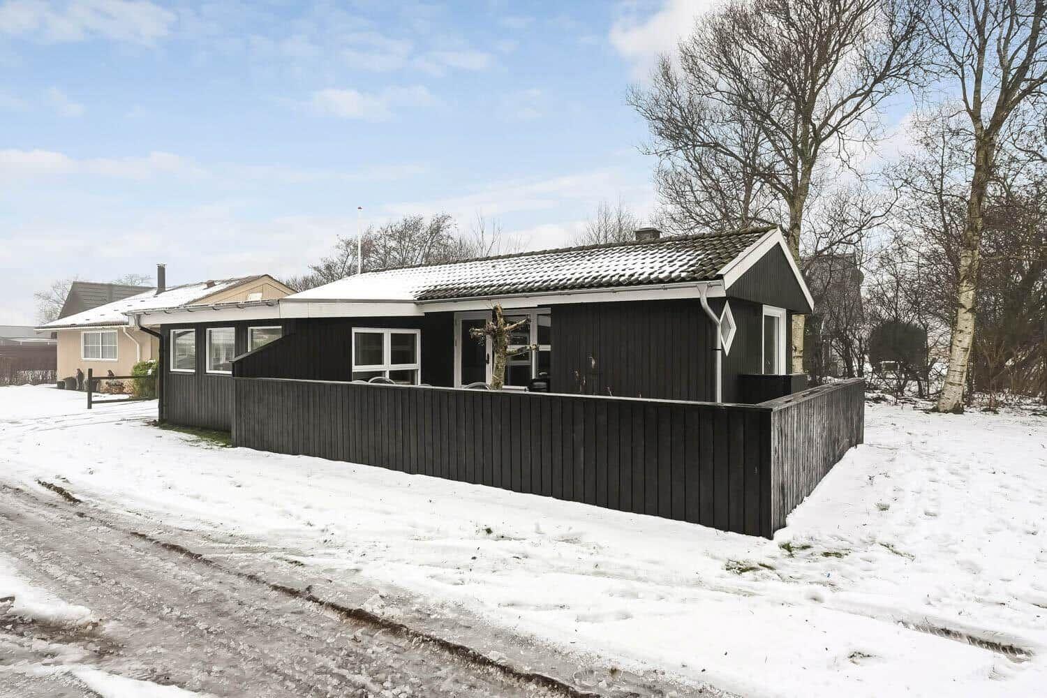 Schwarzes Haus mit Schnee bedecktem Dach und Holzzaun.