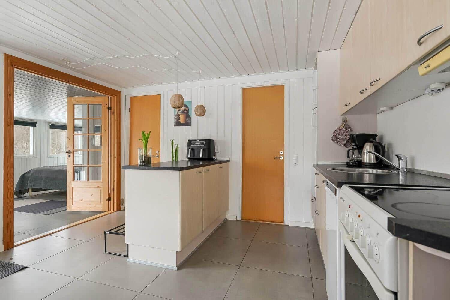 Küche mit Arbeitsplatte, Spüle und Kochfeld. Durchgang zu Schlafzimmer mit Bett.