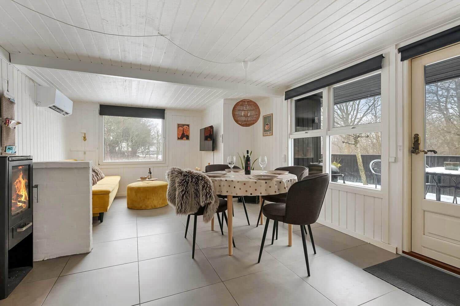 Esszimmer mit runden Tisch, Stühlen und Fensterblick. Kaminofen und gelber Sitzbereich.