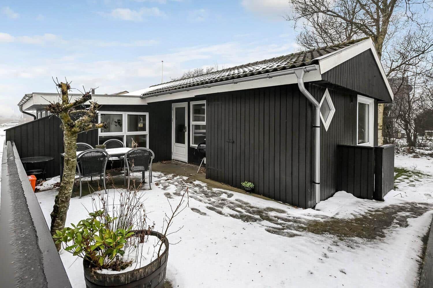 Schwarzes Haus mit weißem Dachrand und Terrasse im Schnee.
