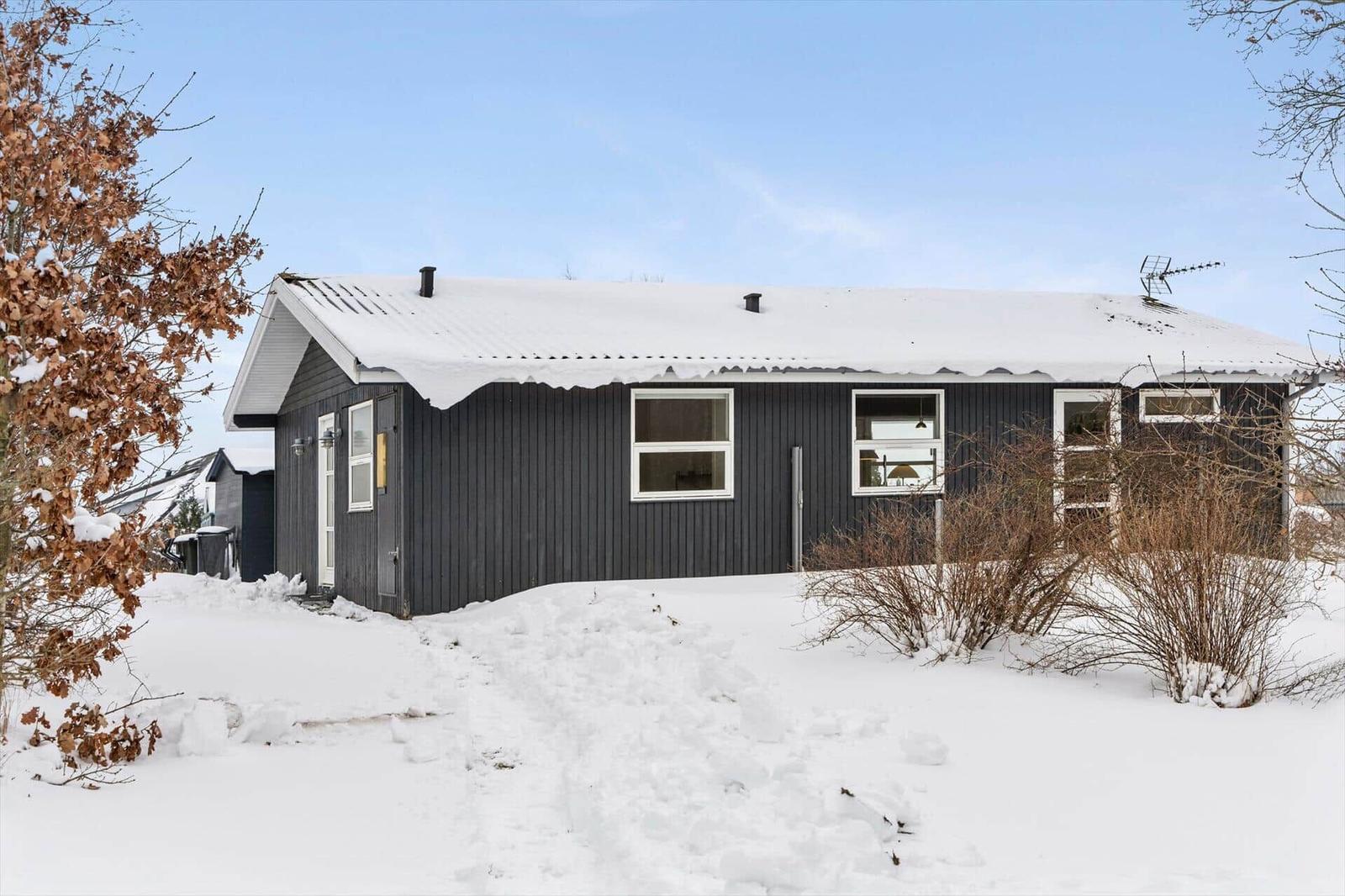 Black wooden house with snow-covered roof and white window frames.